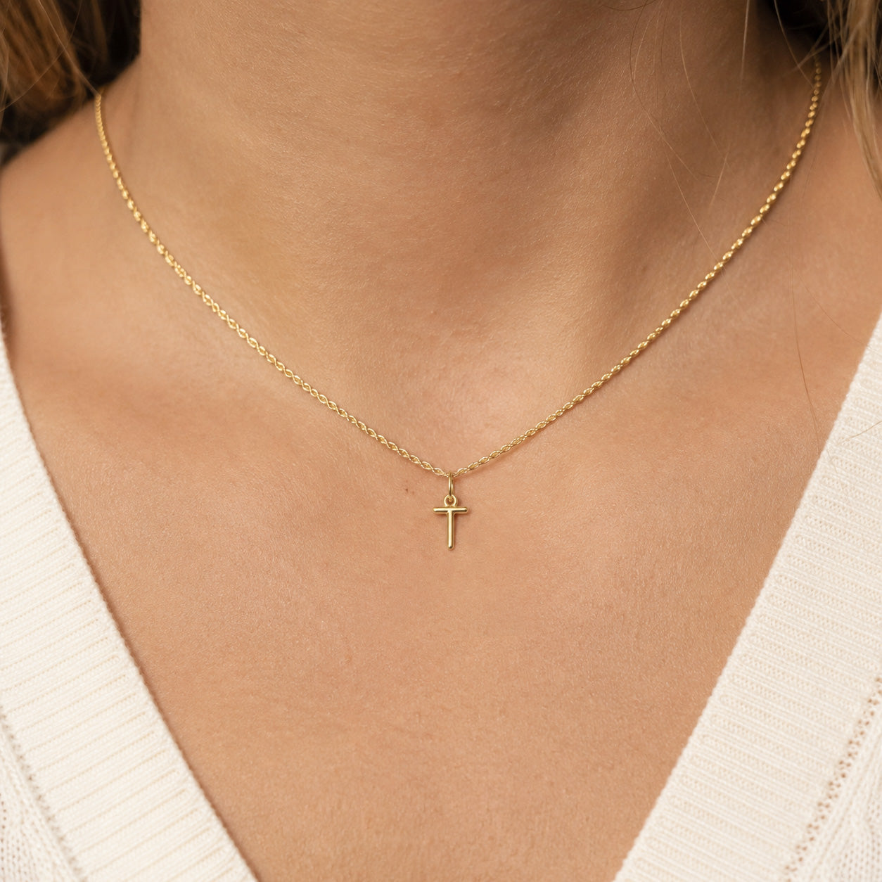 [group: t-10k-gold]A delicate gold chain necklace with a small cross pendant, worn on a model's neck over a white ribbed V-neck top.