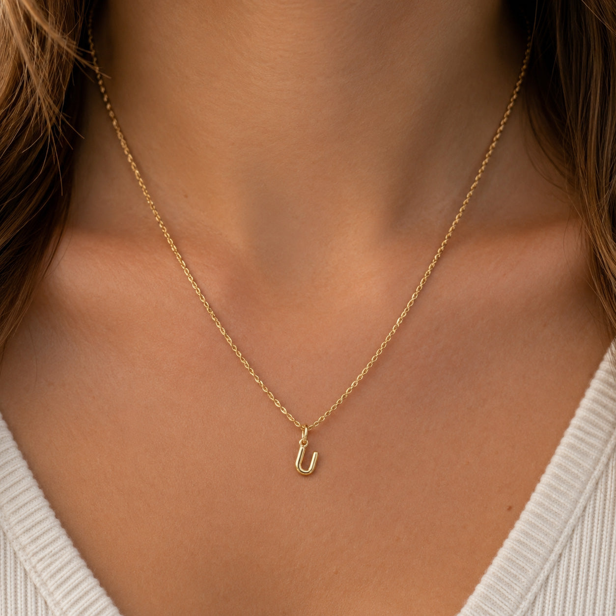 [group: u-10k-gold]A close-up of a model's neck and chest wearing a delicate gold chain necklace with a small U-shaped initial pendant.