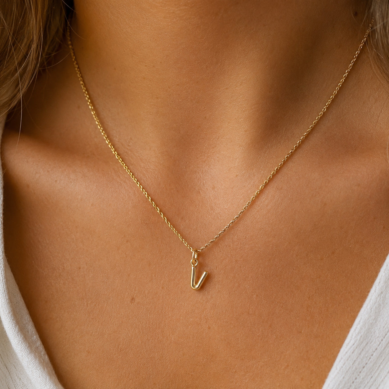 [group: v-10k-gold] A delicate gold chain necklace with a small lowercase letter 'v' pendant, worn on the neck of a model.