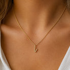 [group: v-10k-gold] A delicate gold chain necklace with a small lowercase letter 'v' pendant, worn on the neck of a model.