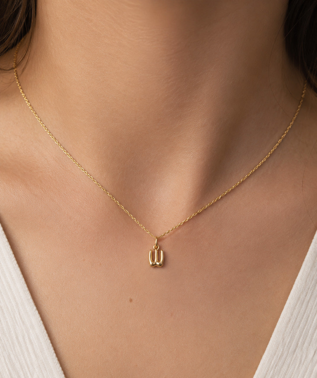 [group: w-10k-gold]A delicate gold chain necklace with a small, minimalist pendant worn by a model. The necklace is shown close-up against the model's neck and upper chest, wearing a white ribbed top.