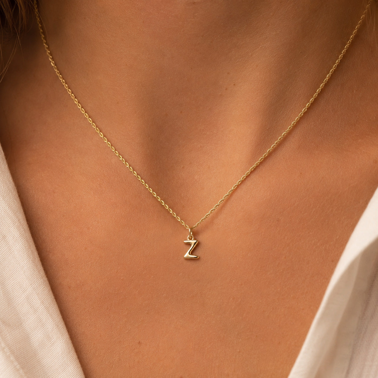 [group: z-10k-gold]A close-up of a person's neck and chest wearing a delicate gold chain necklace with a small capital letter 'Z' pendant.