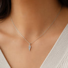 Silver necklace with a feather pendant on a person wearing a light-colored top.