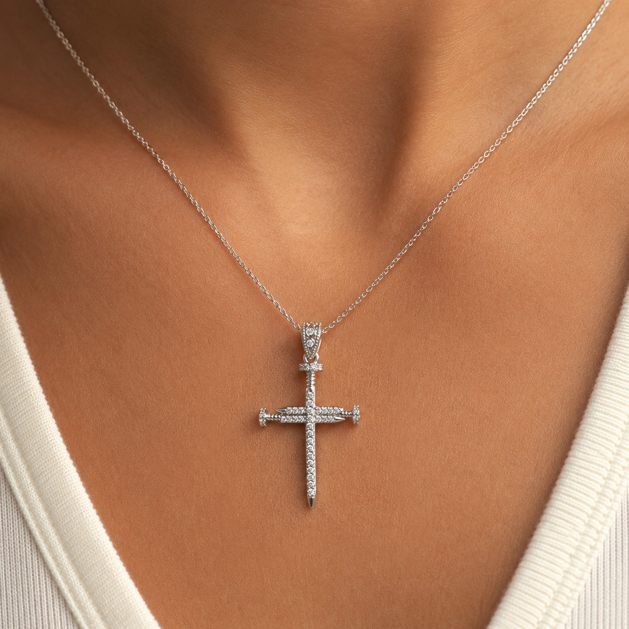 A silver cross pendant necklace with a sword design, worn on a model's neck over a white ribbed top.