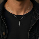 Person wearing a silver cross necklace with a black shirt and dark jacket.