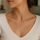 Silver cross necklace on a person wearing a white top
