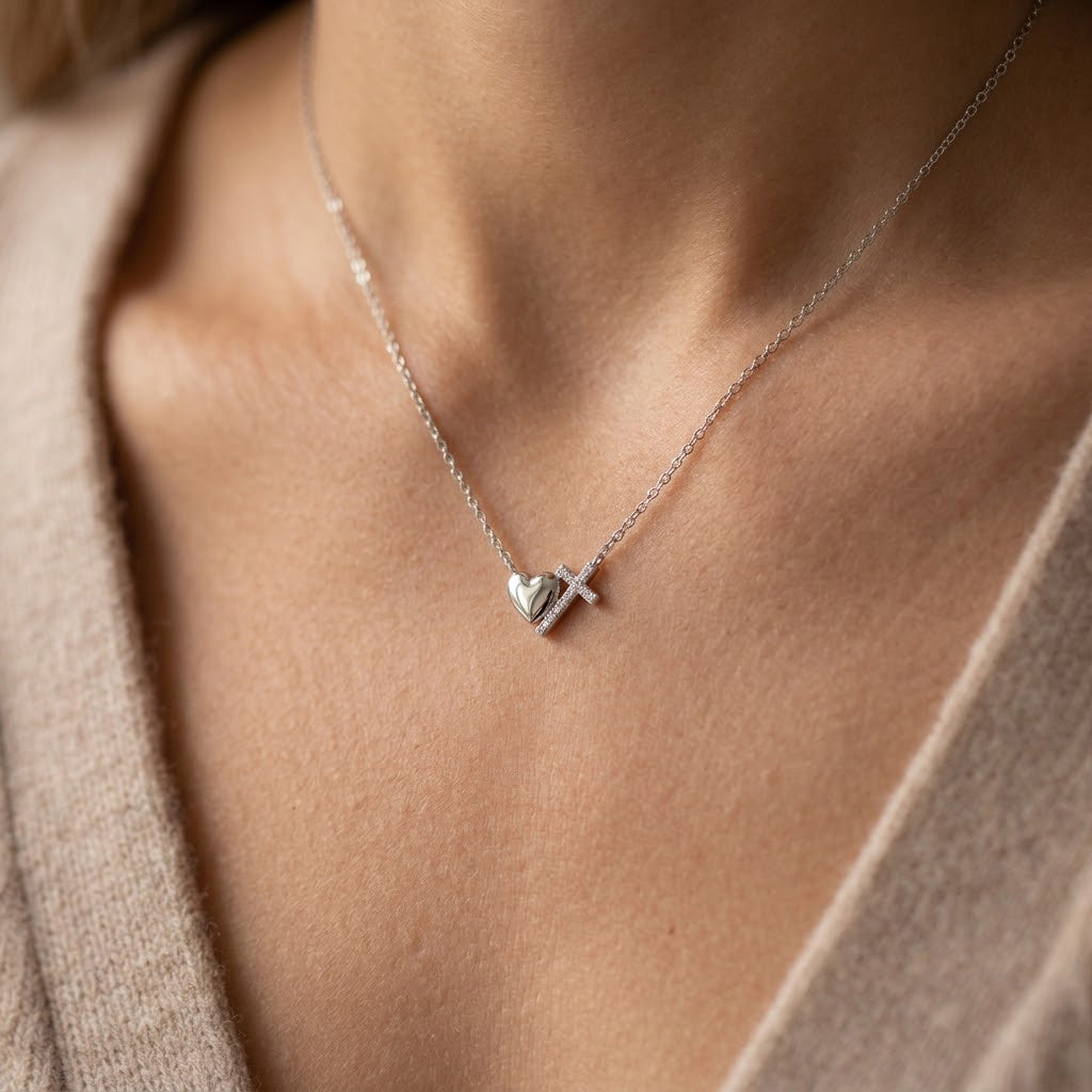 Necklace with a heart and cross pendant on a person wearing a beige sweater.