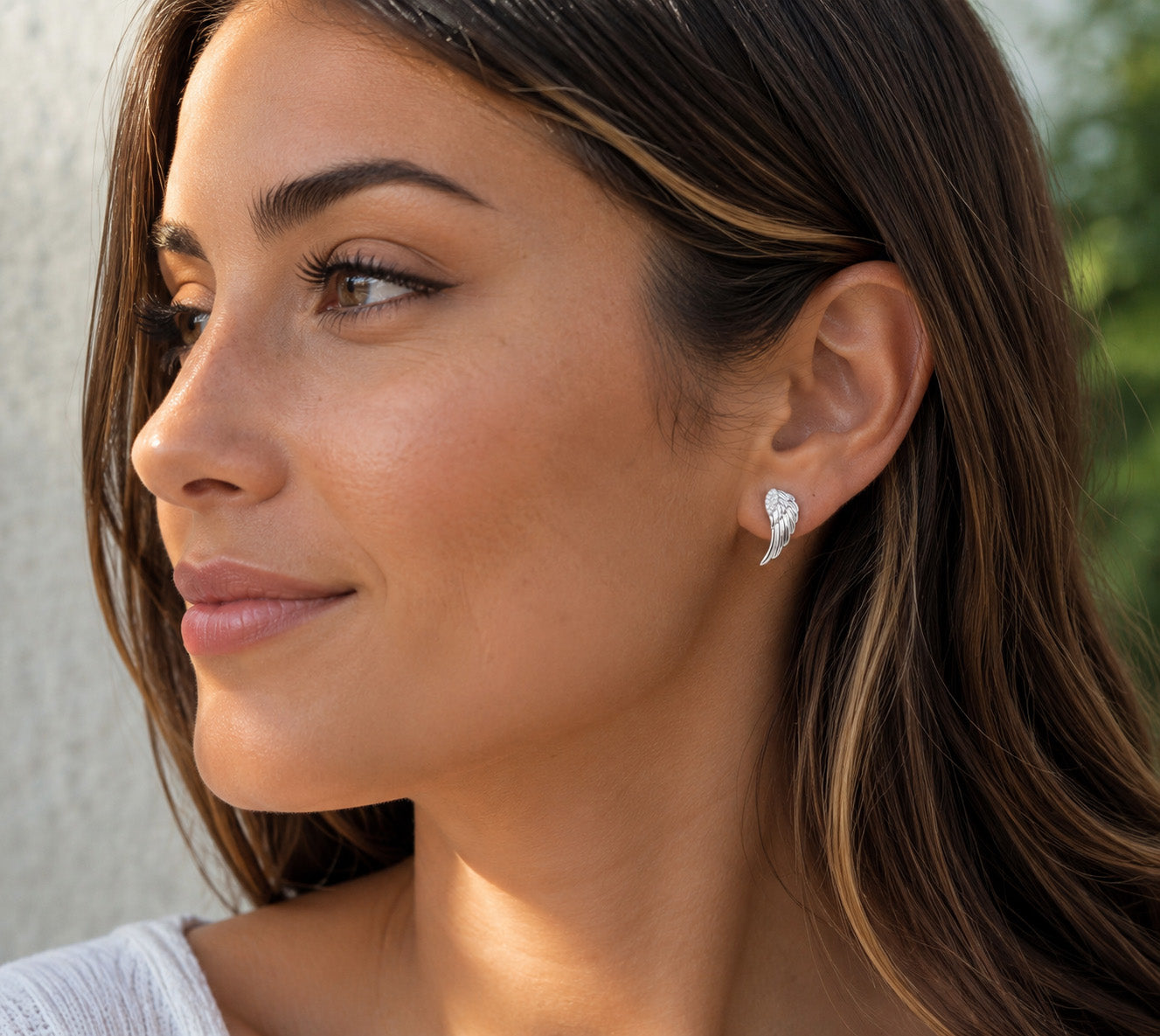 A close-up side profile of a woman with long brown hair wearing a small silver crescent-shaped stud earring with a clear gemstone.