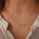 [group: silver]A silver safety pin necklace with small clear stones, worn on a model's neck over a white textured blouse.