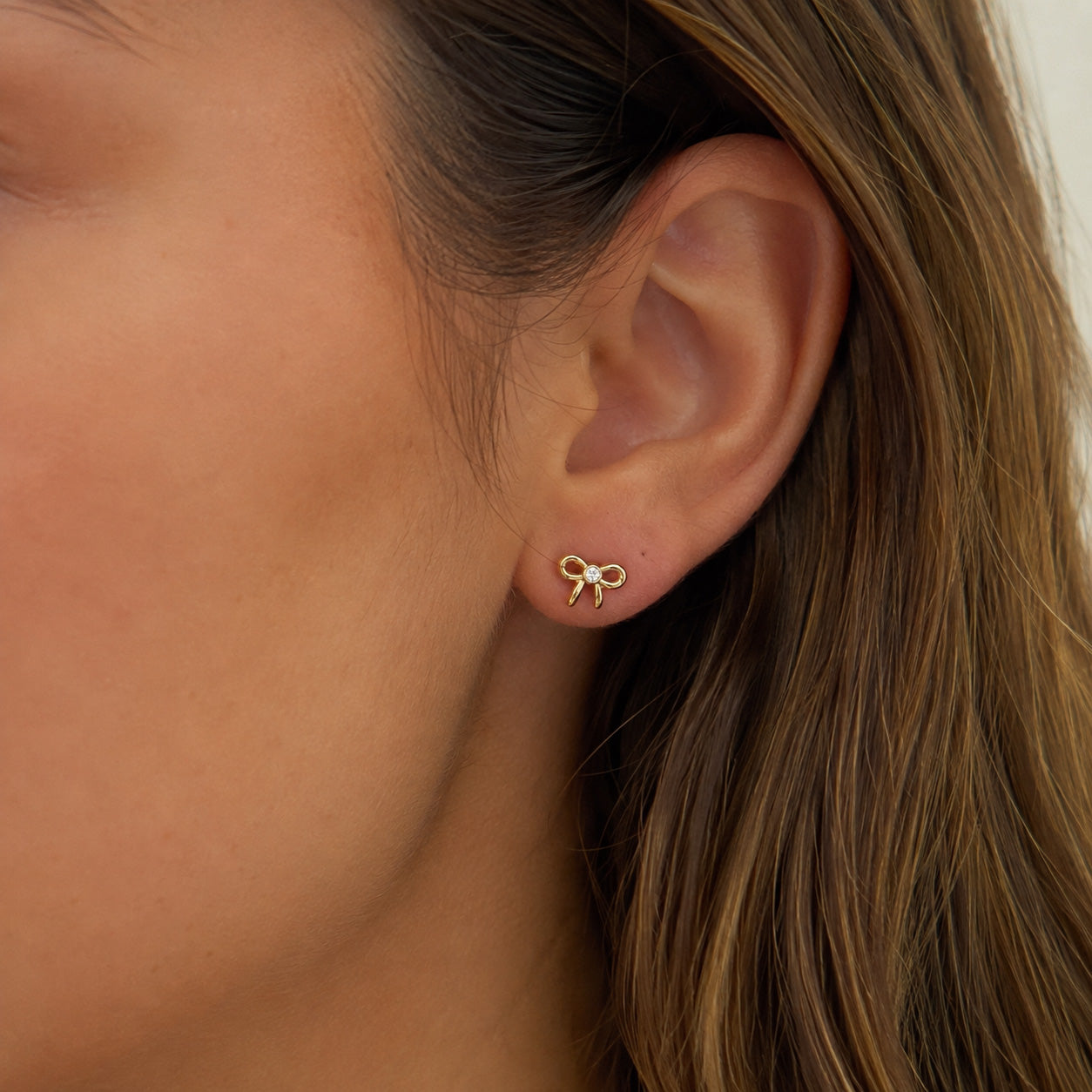A close-up of a person's ear wearing a small gold bow stud earring.
