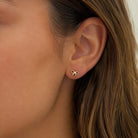 A close-up of a person's ear wearing a small gold bow stud earring.