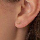 A close-up of a person's ear wearing a small, delicate gold wavy stud earring.