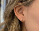 A close-up of a person's ear wearing a small gold stud earring with a textured, circular design.
