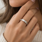 A close-up of a person's hand wearing a polished silver band ring with a small decorative bead detail on one side, set against a soft-focus background of hair and a cream knit sweater.