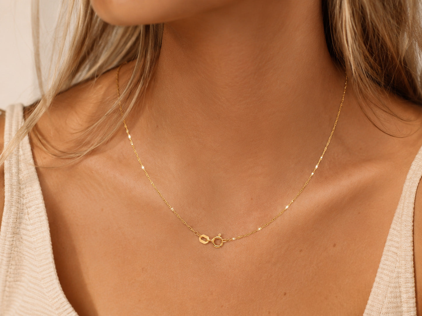 Close-up of a gold necklace on a person wearing a beige top.