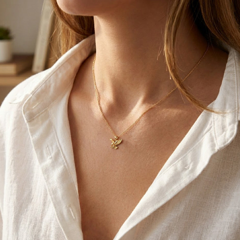 [group:gold-plated-large] Close-up of a person wearing a gold necklace with a dove pendant, against a neutral background.
