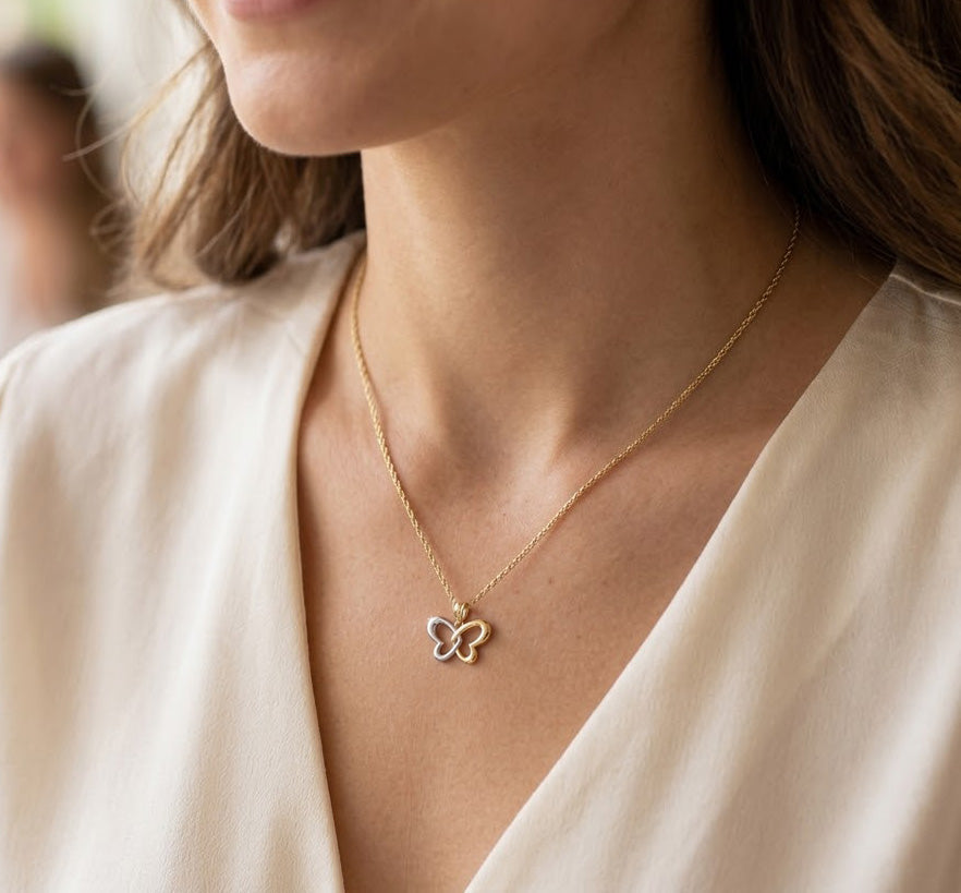 Gold butterfly necklace on a person wearing a white top