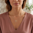 [group: 10k-gold] Woman wearing a gold necklace with a butterfly pendant on a blurred background