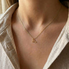 Gold necklace with a leaf pendant worn by a person in a beige shirt.