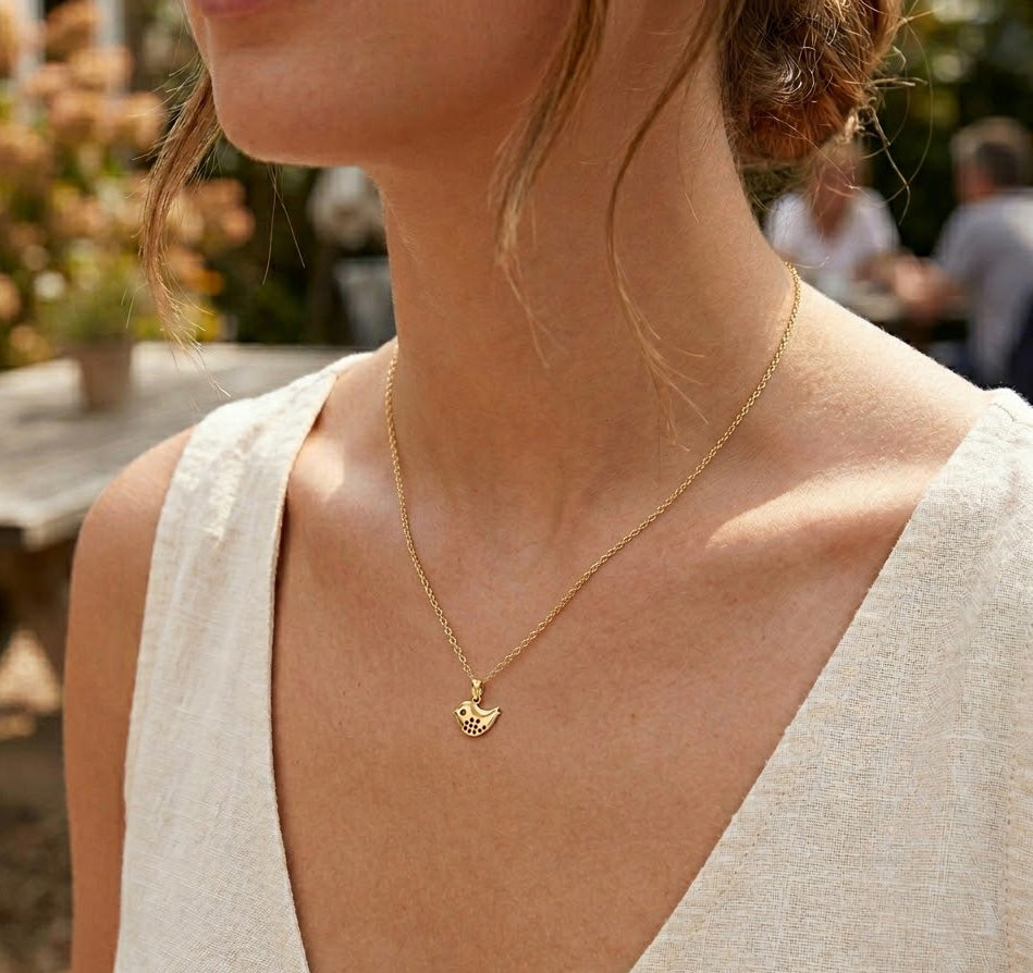 [group:gold-plated]Close-up of a person wearing a gold necklace with a heart pendant outdoors.