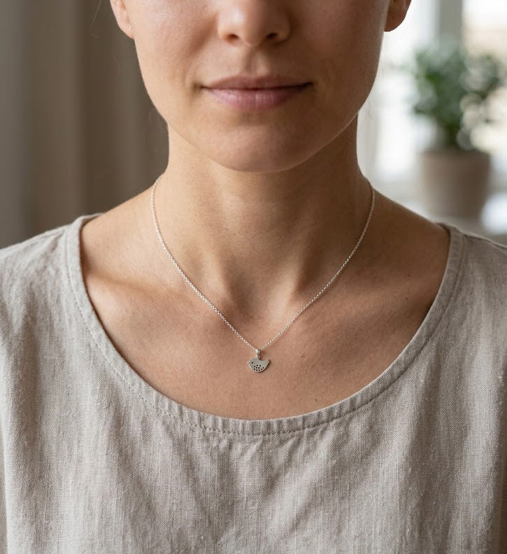 [group:silver] Person wearing a delicate necklace with a heart pendant, blurred background