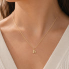 A delicate gold chain necklace with a small swan pendant, worn on a model's neck over a white knit top.