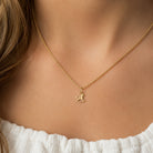 A delicate gold chain necklace with a small horse-shaped pendant, worn by a model in a close-up shot.