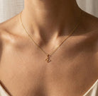 Gold necklace with a butterfly pendant on a person's neck against a neutral background