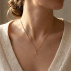 Gold necklace with a giraffe pendant worn by a person in a neutral setting