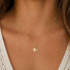 A delicate gold chain necklace with a small bird-shaped pendant, worn on the neck of a model wearing a white knit top.