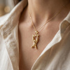 Gold necklace with a pendant worn by a person against a neutral background
