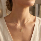 A close-up of a woman wearing a delicate gold chain necklace with a lion head pendant, styled with a cream-colored top.