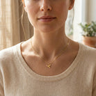 Woman wearing a gold necklace with a delicate dove pendant, set against a neutral background.