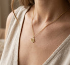 Close-up of a person wearing a gold necklace with a spiral pendant.