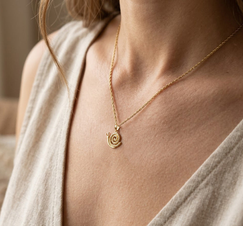 Close-up of a person wearing a gold necklace with a spiral pendant.