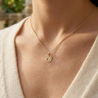 Gold necklace with a pendant on a person wearing a light-colored top.