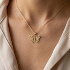Gold butterfly necklace on a person wearing a beige top