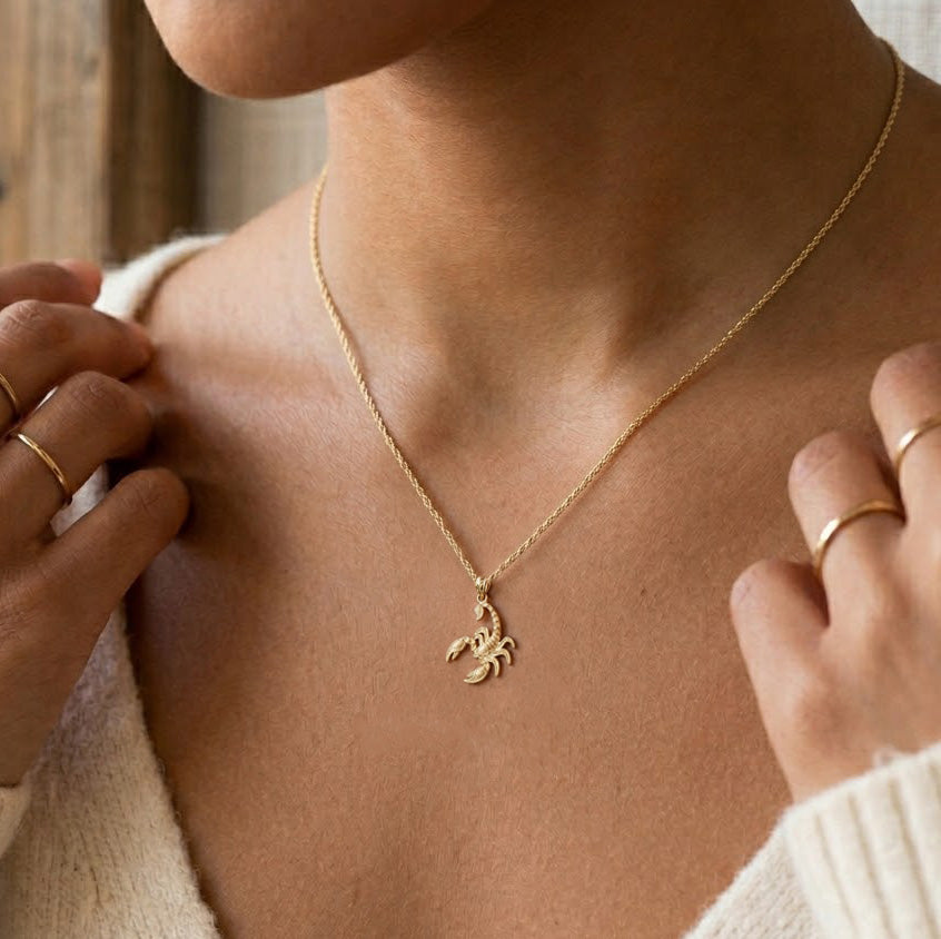 Person wearing a gold necklace with a scorpion pendant.