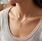 Gold necklace with a small pendant worn by a person in a gray sweater.