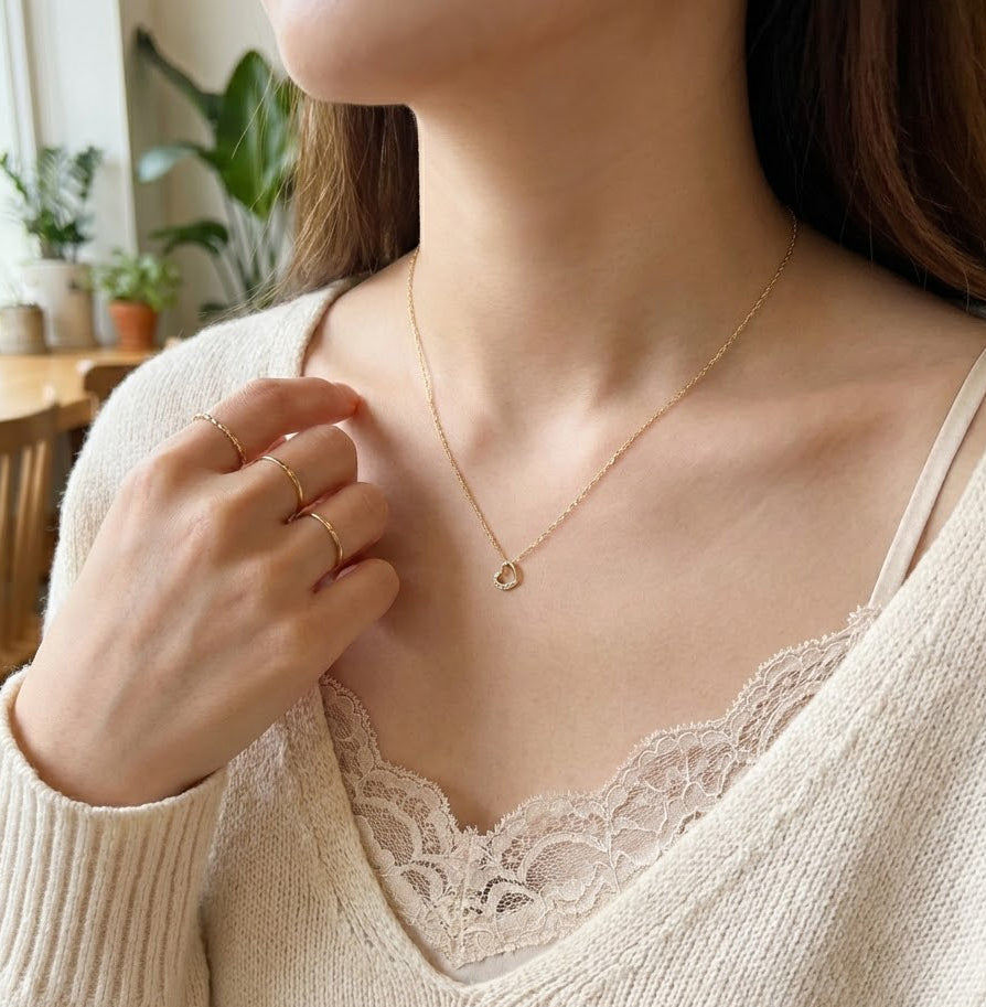 Close-up of a person wearing a delicate gold necklace and rings, with a blurred indoor background.