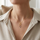A close-up of a model wearing a delicate gold chain necklace with a multi-heart pendant in gold, rose gold, and silver, styled with a beige linen shirt.