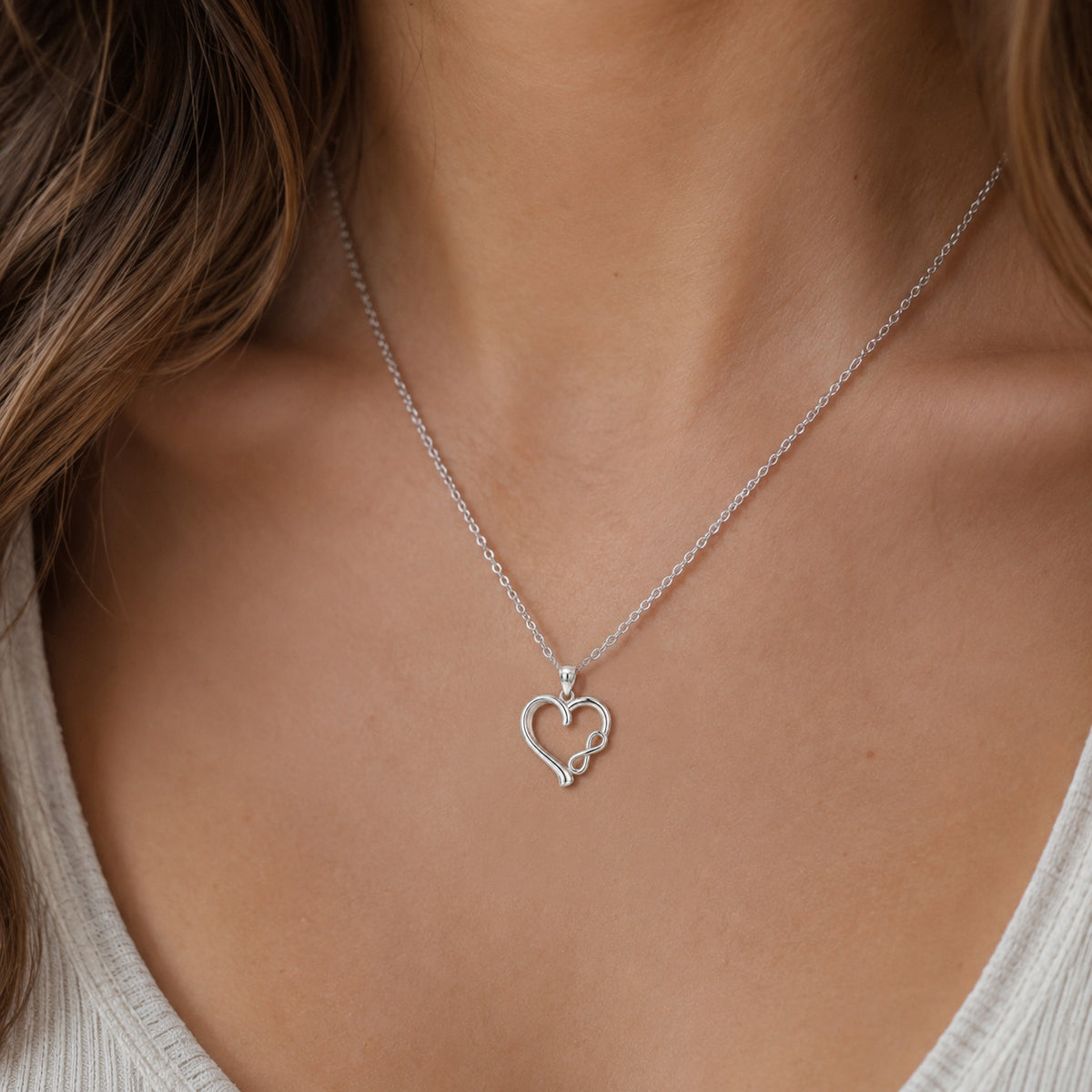 [group: silver] A close-up of a person's neck and chest wearing a delicate silver chain necklace with an open heart-shaped pendant.