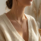 [group: f-10k-gold]A close-up lifestyle shot of a woman wearing a delicate gold chain necklace with a small key pendant, styled with a cream-colored knit cardigan.