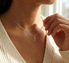 [group: g-10k-gold] A close-up lifestyle shot of a model wearing a delicate gold chain necklace with a small cursive initial 'G' pendant, styled with a cream ribbed knit top.