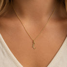 [group: l-10k-gold]A delicate gold chain necklace with a small cursive initial pendant, shown worn on a model's neck over a cream-colored V-neck top.