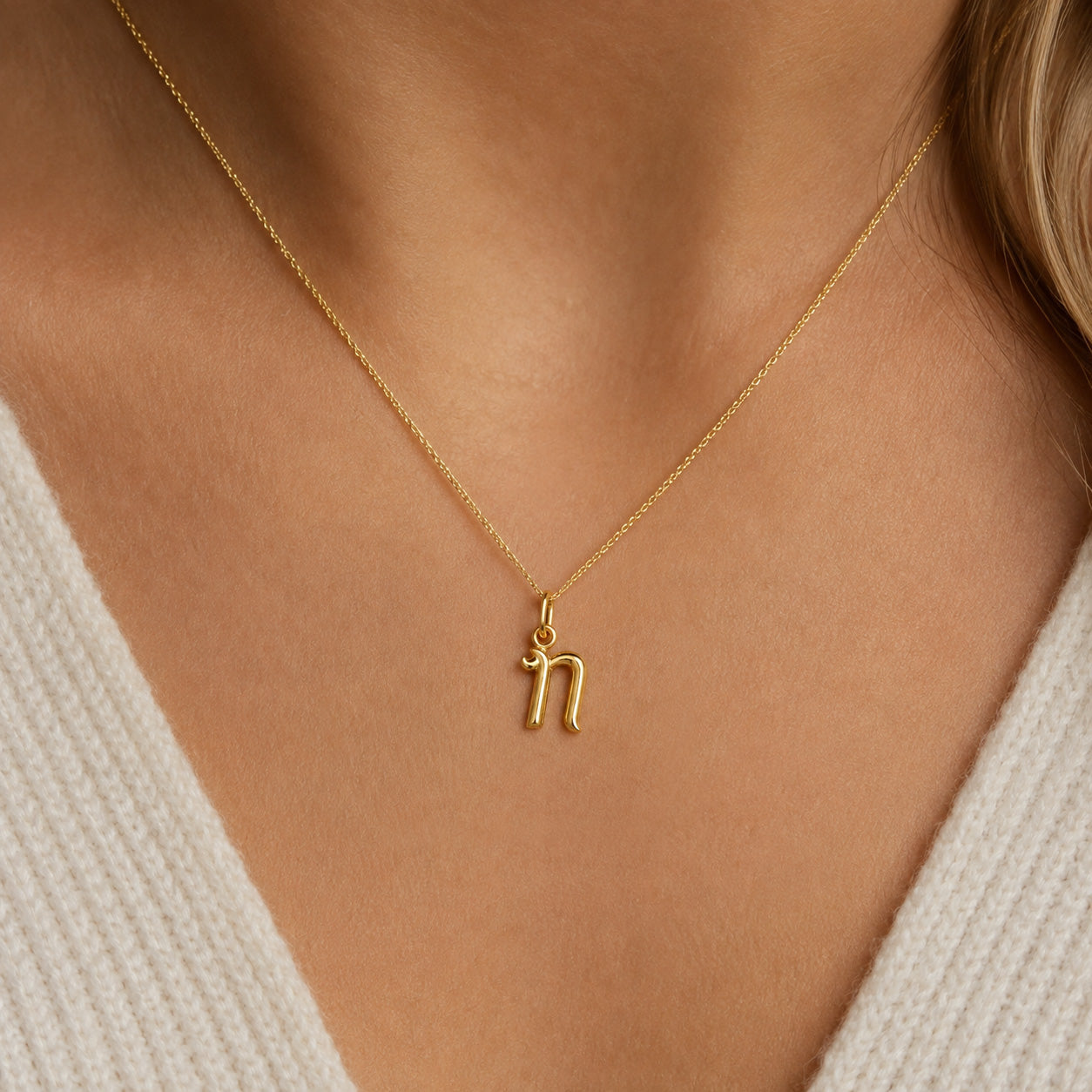 [group: n-10k-gold]A close-up of a model wearing a delicate gold chain necklace with a small lowercase letter 'n' pendant.