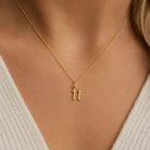 [group: n-10k-gold]A close-up of a model wearing a delicate gold chain necklace with a small lowercase letter 'n' pendant.