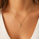 [group: p-10k-gold]A close-up of a model wearing a delicate gold chain necklace with a small, stylized lowercase 'p' pendant, paired with a white ribbed top.