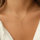 [group: q-10k-gold]A delicate gold chain necklace with a small cursive initial pendant, worn on a model's neck over a white knit top.