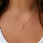 [group: r-10k-gold]A delicate gold chain necklace with a small, abstract curved gold pendant, shown worn on a model's neck over a white ribbed top.